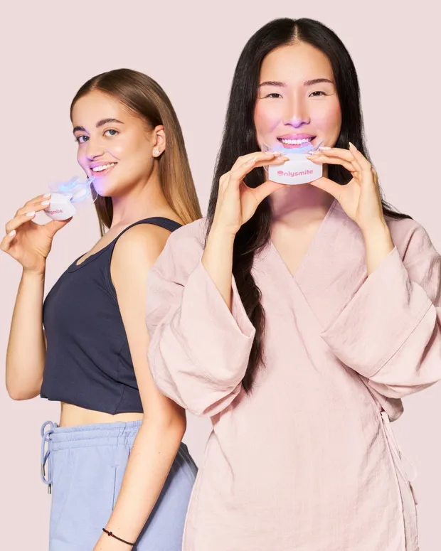Lächelnde Frau hält eine Onlysmile-Mundschiene mit LED-Licht und das Zahnaufhellungsgel